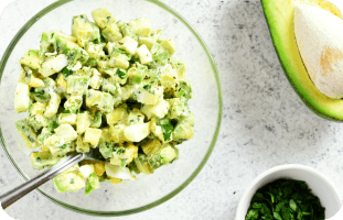 Bowl of avocado egg salad with chopped herbs and avocado halves